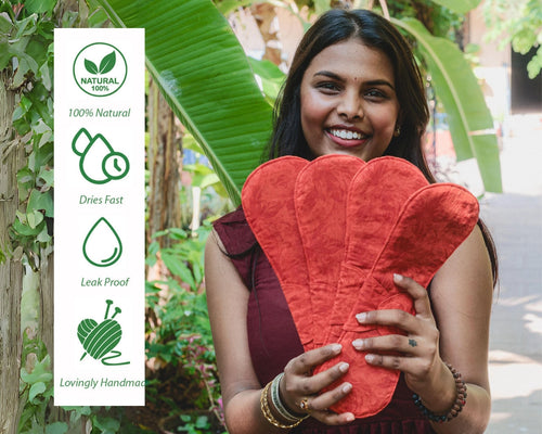 A woman smiling, holding an eco-friendly sanitary pad while standing in a lush garden with banana plants, promoting the "100% Natural", "Dries Fast", "Leak Proof", "Lovingly Handmade".