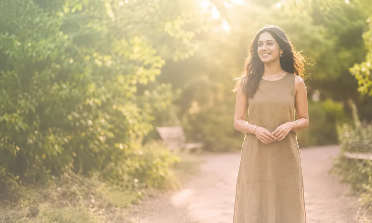 Woman walking outdoors in nature surrounded by greenery and warm sunlight