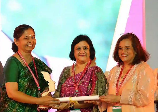 Three women presenting and receiving an award at an event.